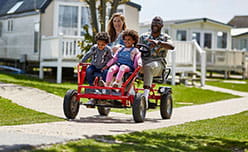 Camber Sands hero image of family riding karts through the caravan park
