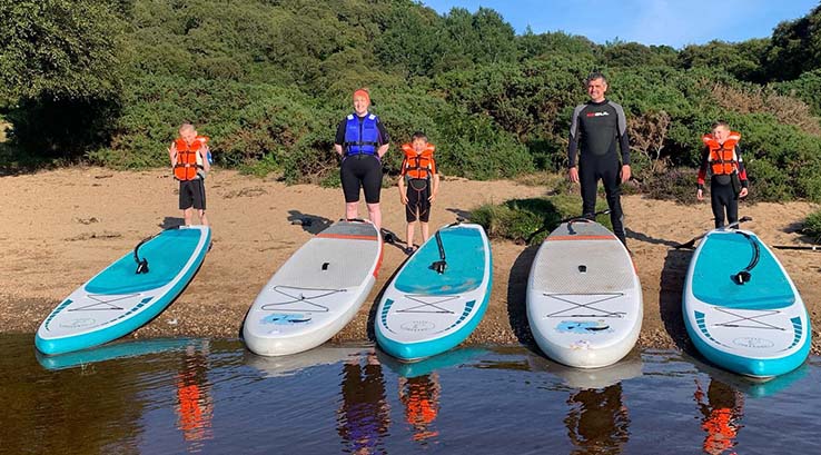 A family getting ready for a paddleboarding lesson on the shore