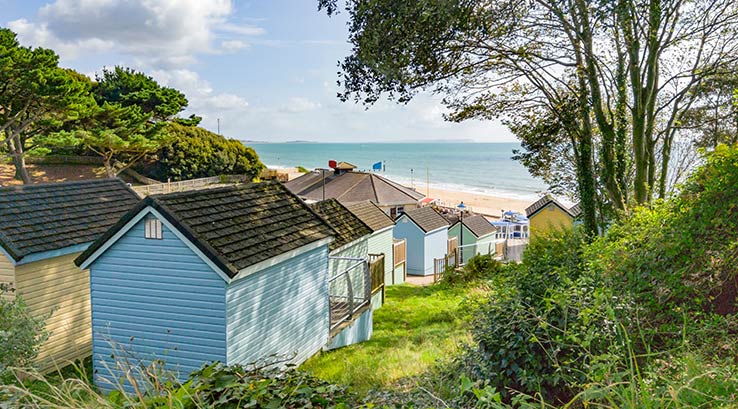 colourful beach huts on a cliff looking towards the beach