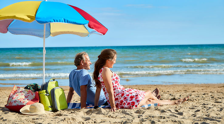 A couple sunbathing on the sand under an umbrella on Camber Sands Beach
