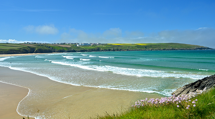 Clifftop view of sunny Crantock beach with waves rolling in