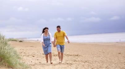 A couple holding hands walking along Heacham Beach