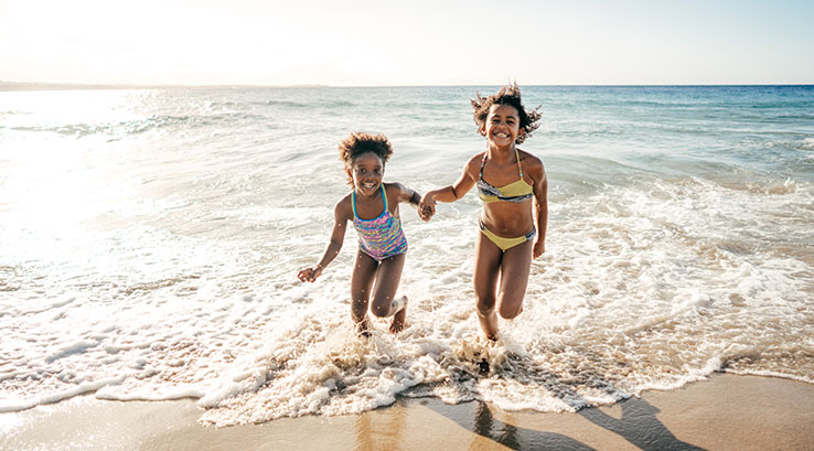 two young girls holding hands running out of the sea