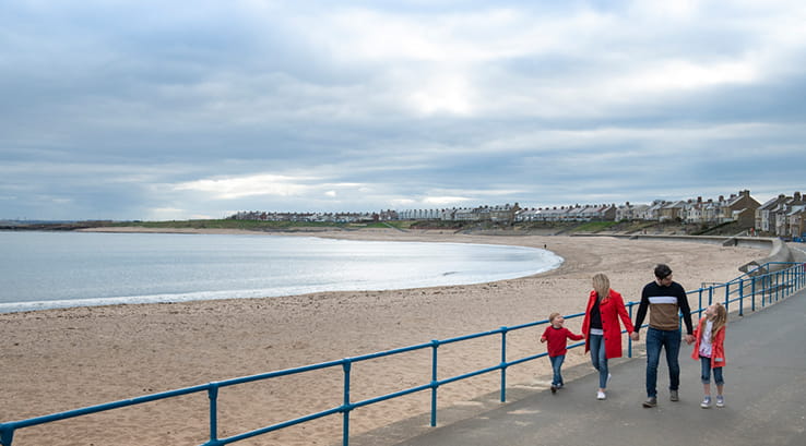 A family walking along the promenade by the beach at Newbiggin-by-the-Sea
