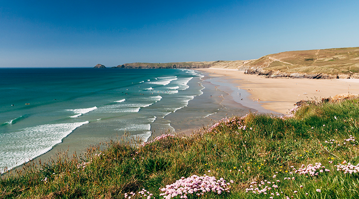 clifftop view of waves rolling into perranporth beach on a sunny day