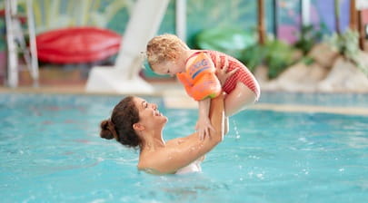A mother lifting her little girl in the air in a swimming pool