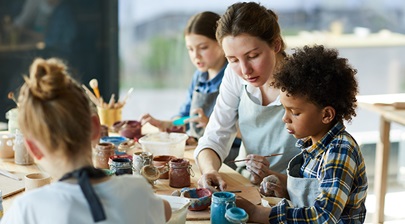 Kids painting pottery, supervised by an adult