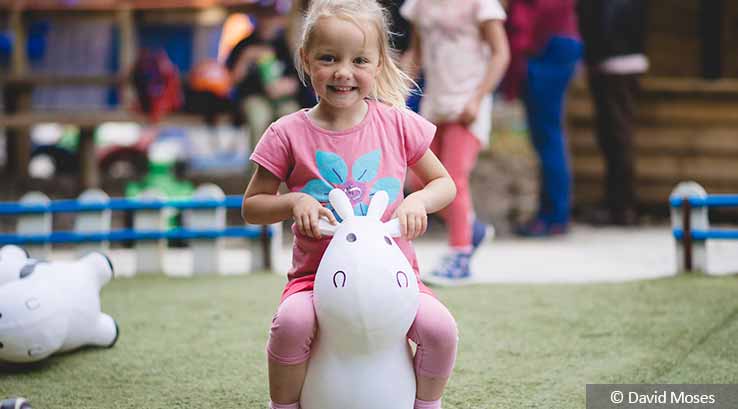 Little girl wearing pink flower t-shirt on a white unicorn