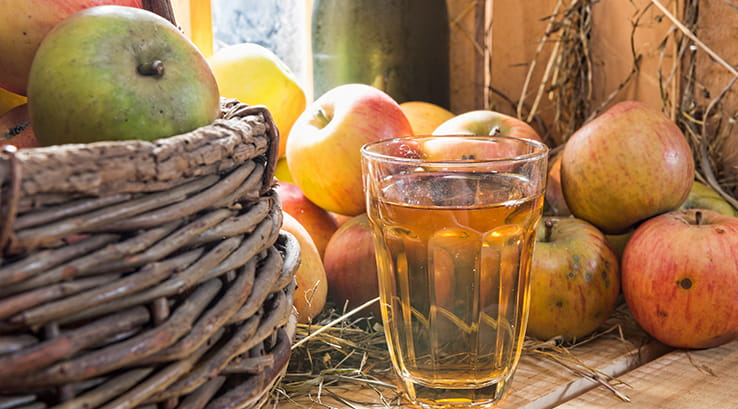 glass of cider next to a basket of apples
