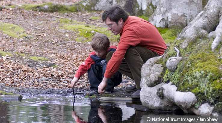 father and young son bending down to a pond in woodland