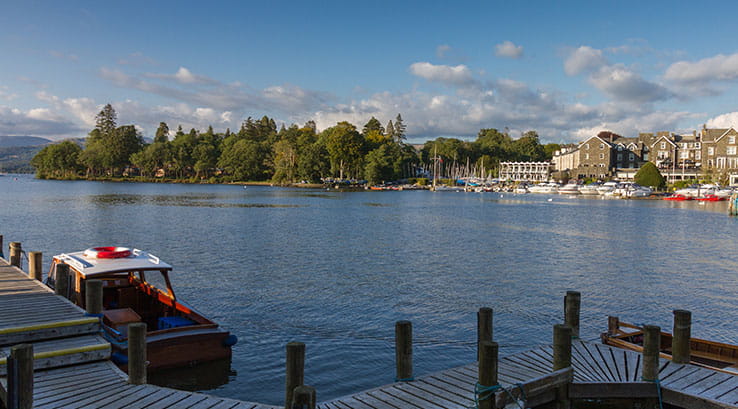 A jetty and boat on Lake Windermere with the town of Bowness in the background