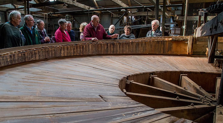 people looking at a large wooden wheel used in mining
