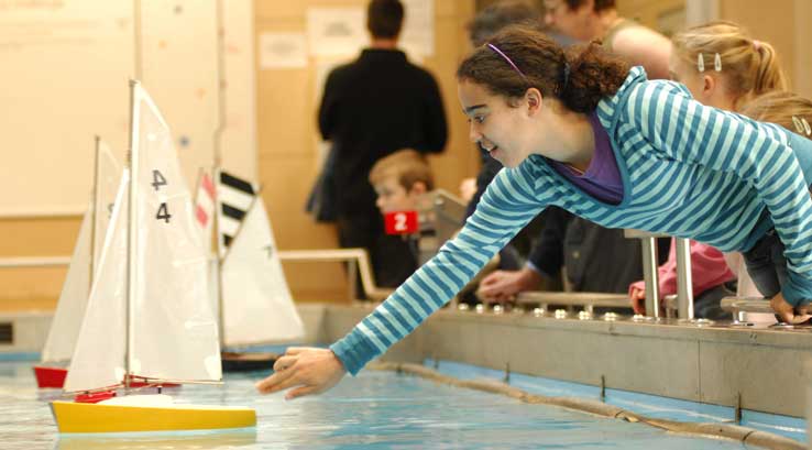 girl pushing a model sail boat in a pool