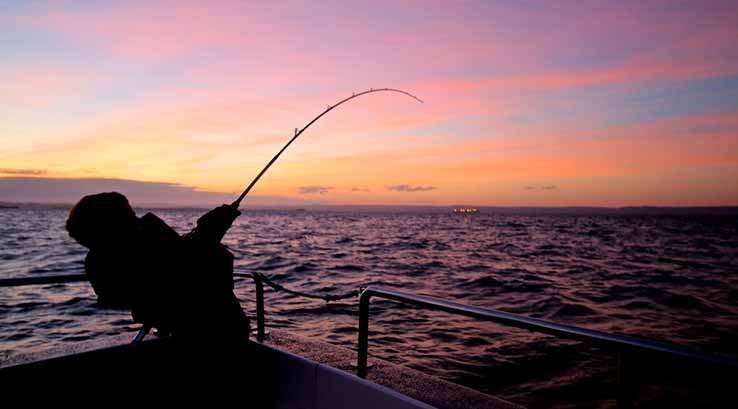 silhouette of man pulling in a catch at sunset