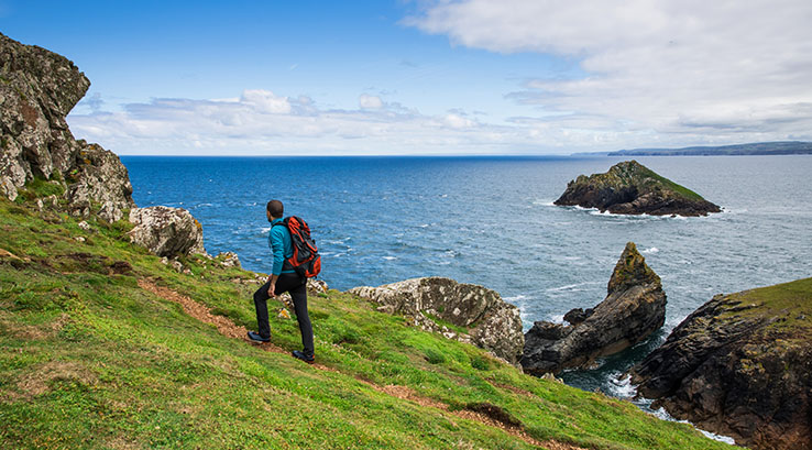 man walking up a coastal hill with cliffs and sea in the distance
