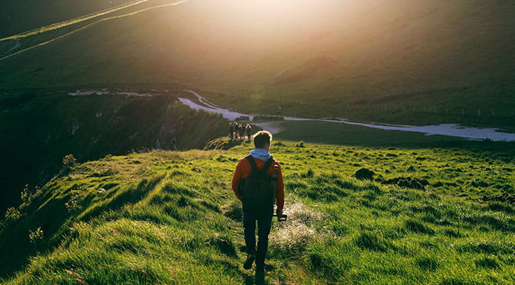 a man walking through a field towards the setting sun