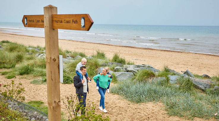 parents carrying toddlers on their backs walking past a sign post