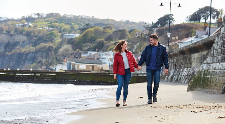 A couple walking along the sand holding hands at Shanklin Beach