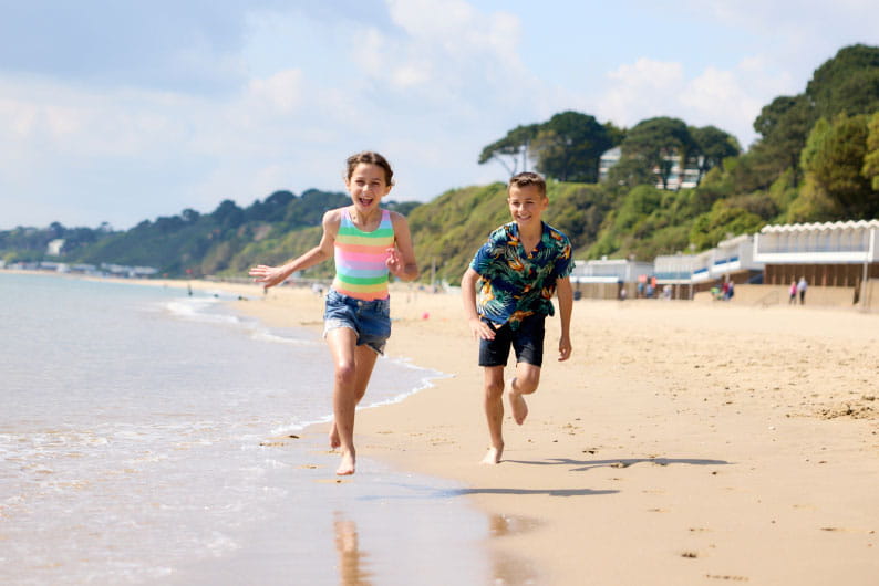 two children running along a sunny, sandy beach