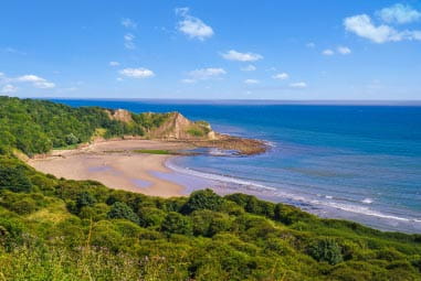Cayton Bay in the sunshine with its greenery, golden sands and blue waters
