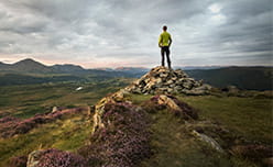 A hiker standing on rocks overlooking the hills of the Lake District