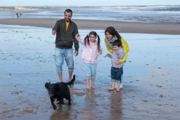 Family stood on the beach looking at pet dog