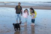 Family stood on the beach looking at pet dog