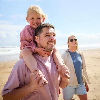 Couple walking on a beach with a toddler on shoulders