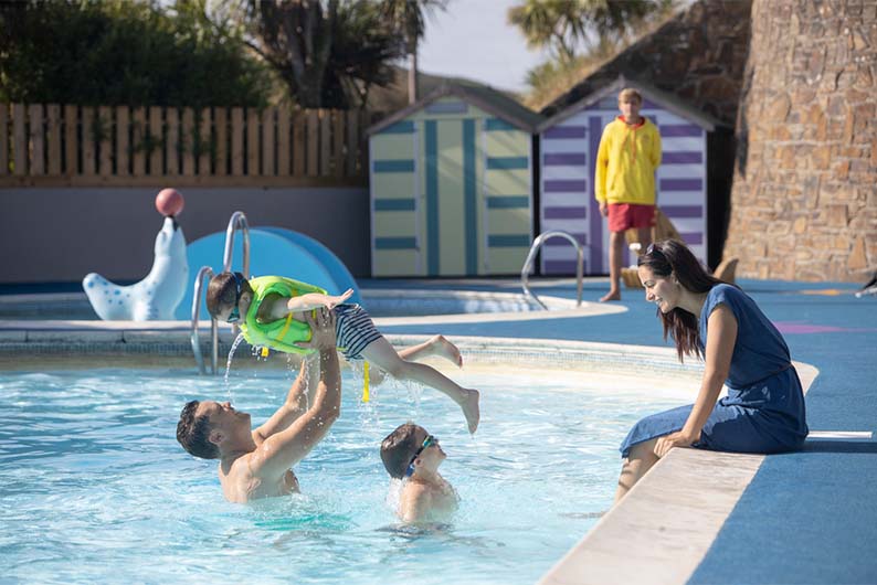 A family playing in an outdoor swimming pool on a Parkdean Resorts holiday park
