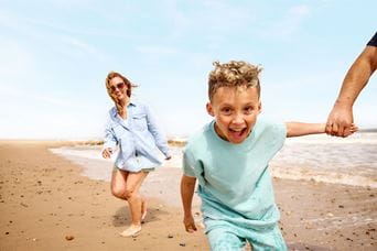 A kid running along the beach holding hands with a parent