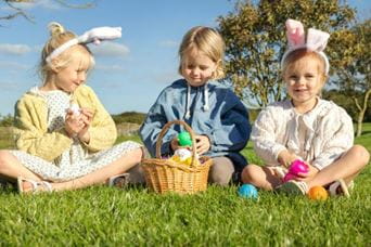 Three little girls wearing bunny ears eating choccie eggs
