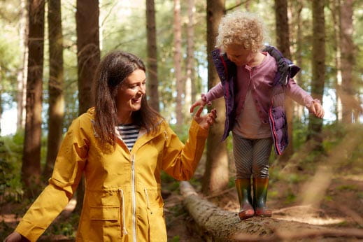 Mum holding daughters hand walking through woods
