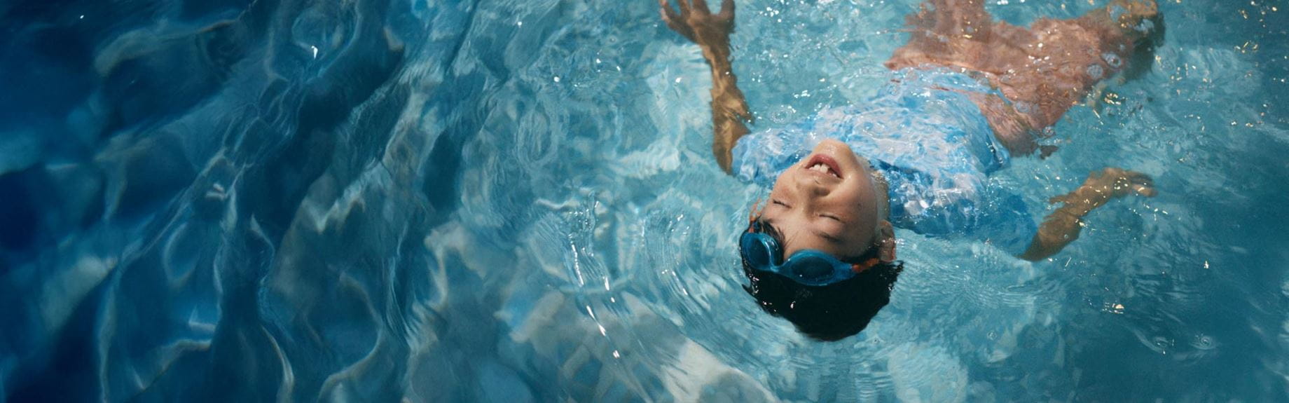 Little boy lying on back in the swimming pool smiling