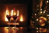 Two wine glasses filled with red wine with roaring fire in background