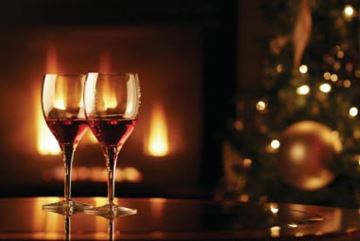 Two wine glasses filled with red wine with roaring fire in background