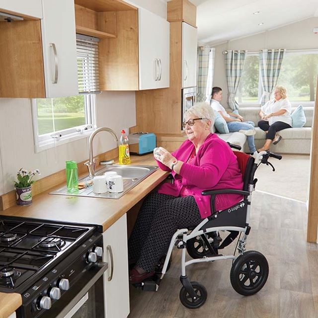 A woman in a wheelchair drying dishes in the kitchen of an accessible caravan
