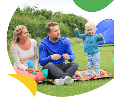 Parents with a young child sat outside their tent on the touring and camping field at Breydon Water Holiday Park