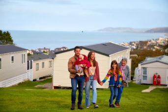 Young couple and their three kids walking with holiday park in the background