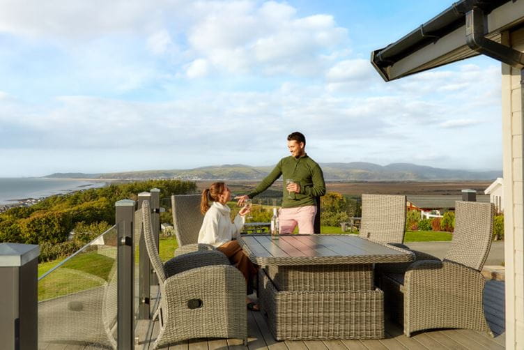 A man and woman sat outside a lodge with the countryside view in the background