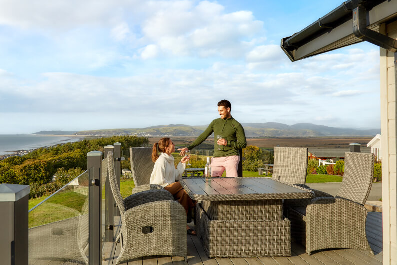 A man and woman sat outside a lodge with the countryside view in the background