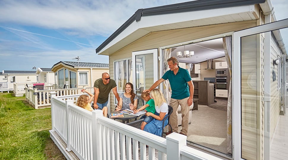A family relaxing on their lodge veranda on a sunny day at Camber Sands Holiday Park