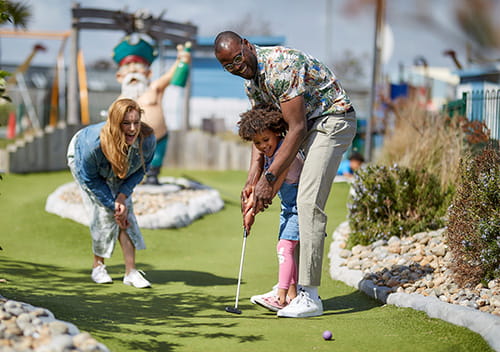 family playing crazy golf putting the ball into the hole