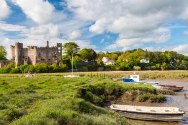 boats moored alongside green fields and an ancient castle