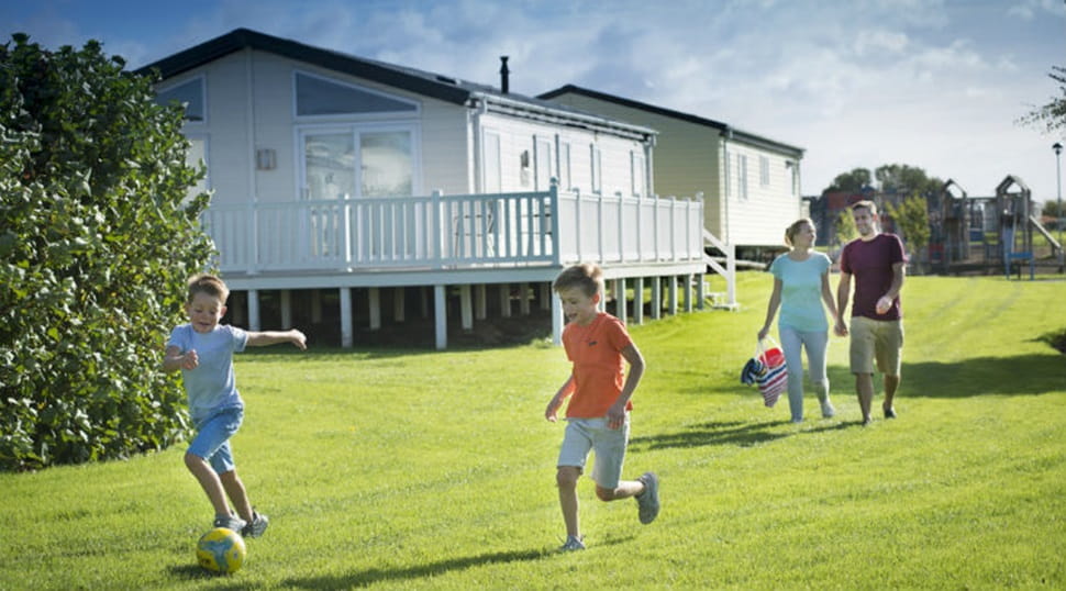 Kids playing football on the grass and parents walking by the caravans at Cayton Bay Holiday Park