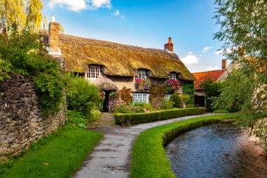 a quaint thatched cottage with a river running past it