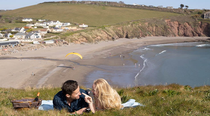 A couple enjoying a picnic on the grassy cliffs overlooking Challaborough Bay Beach