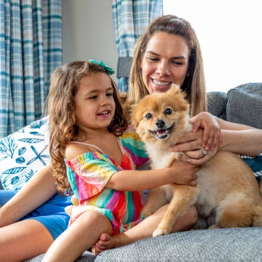 Mother and daughter petting small tan dog on sofa