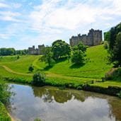 Lush green courtyard and still lake leading up to stony historic period building