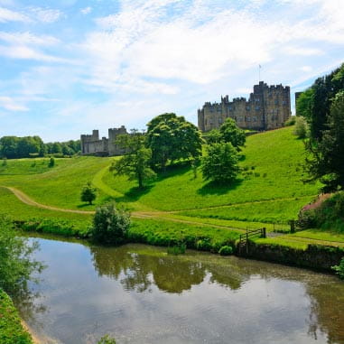 Lush green courtyard and still lake leading up to stony historic period building