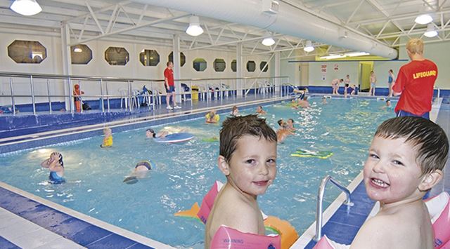Two kids smiling into the camera at the indoor swimming pool